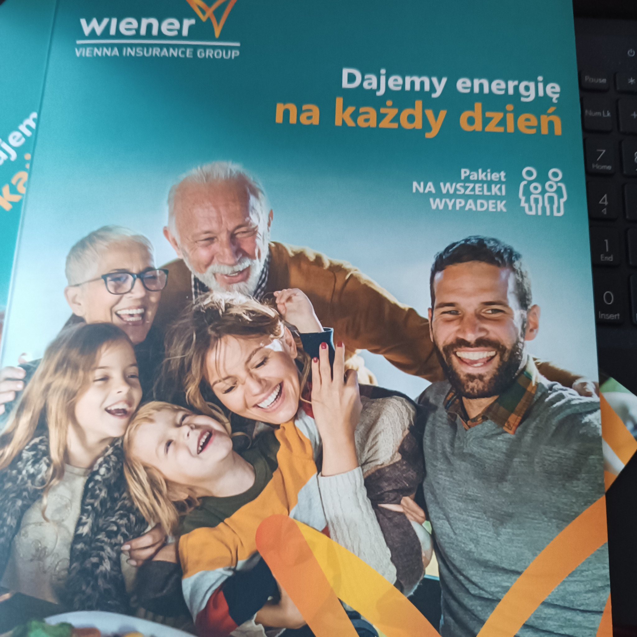 Uśmiechnięta wielopokoleniowa rodzina z okładki folderu reklamowego Wiener Vienna Insurance Group, z hasłem 'Dajemy energię na każdy dzień' i symbolem pakietu ubezpieczeniowego 'Na wszelki wypadek'.