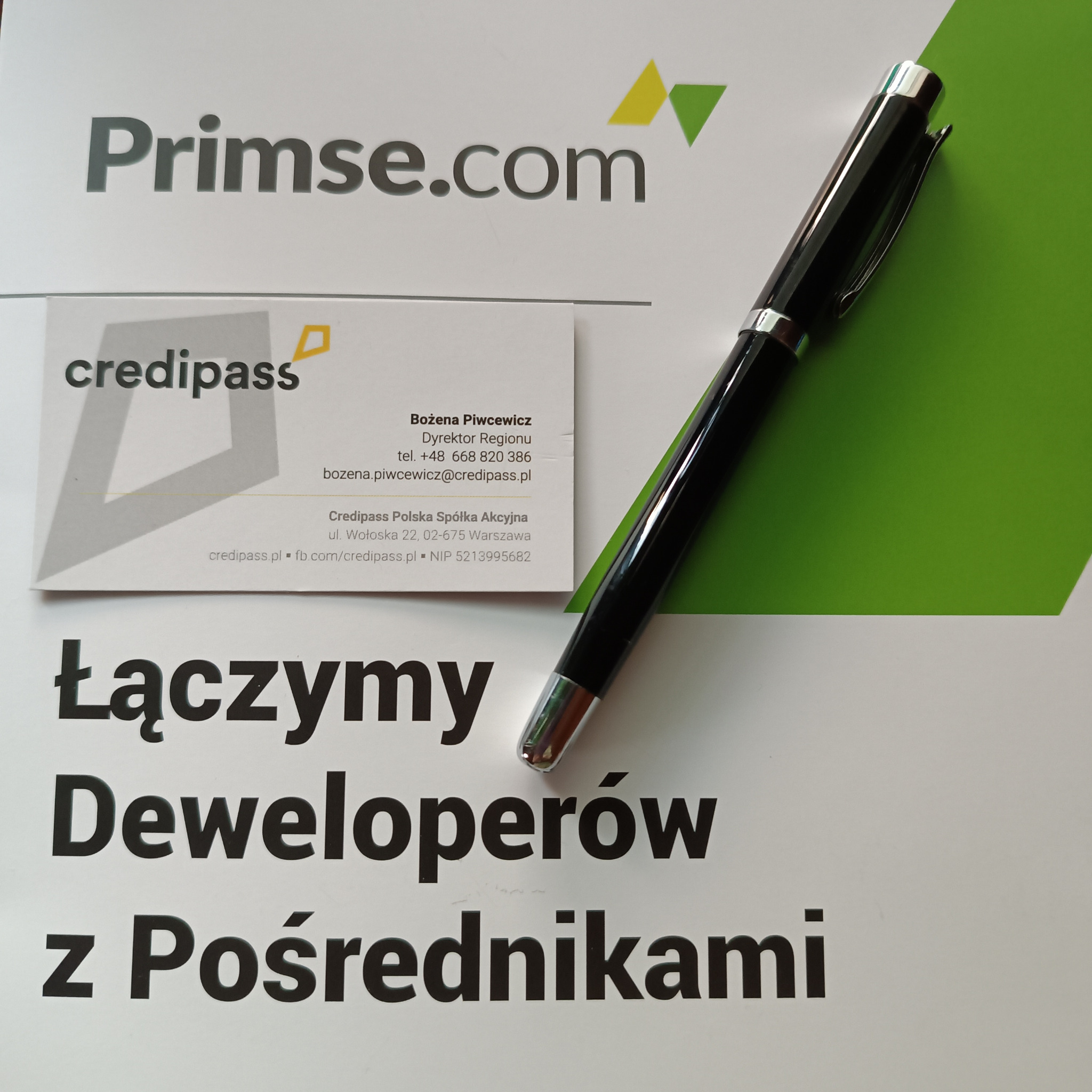 Wizytówka firmy Credipass, długopis i fragment plakatu z hasłem 'Łączymy Deweloperów z Pośrednikami' na białym tle z zielonym akcentem.