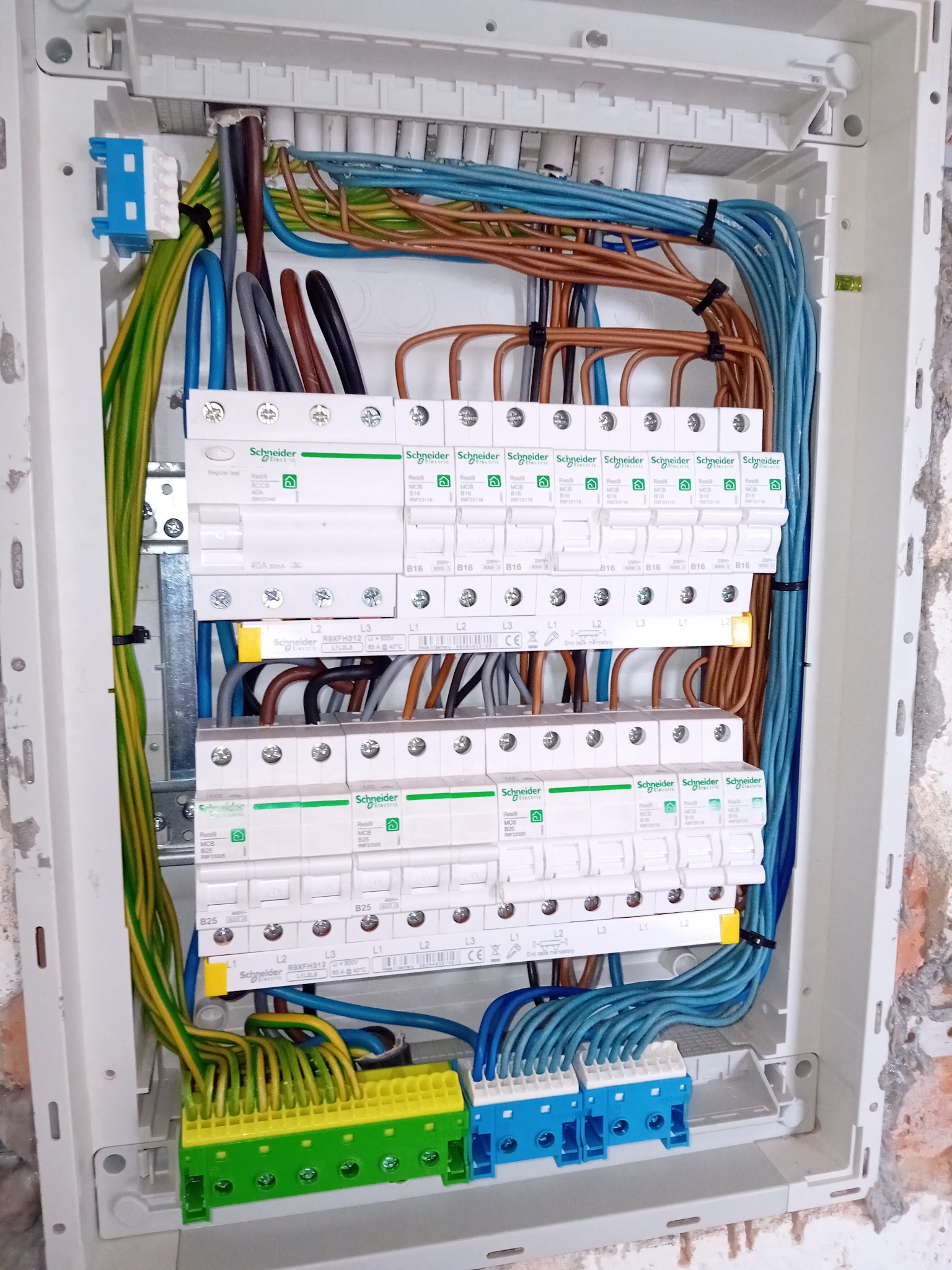 Rozdzielnia elektryczna w trakcie montażu, widoczne zabezpieczenia Schneider Electric, przewody w różnych kolorach, zamocowane w białej obudowie.