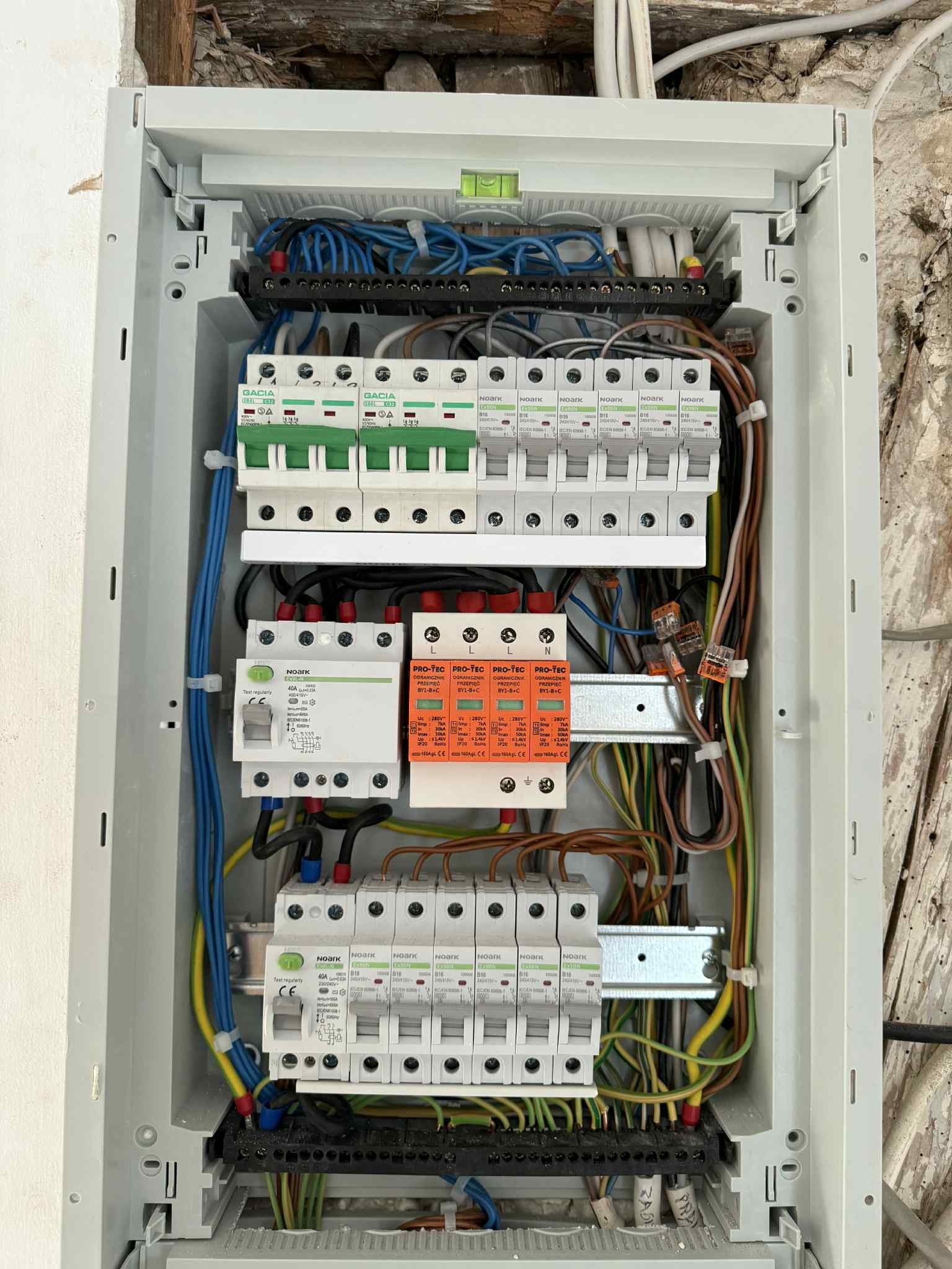 Otwarta skrzynka elektryczna z bezpiecznikami, przewodami i listwami zaciskowymi. Widoczne różne komponenty instalacji elektrycznej wewnątrz skrzynki.