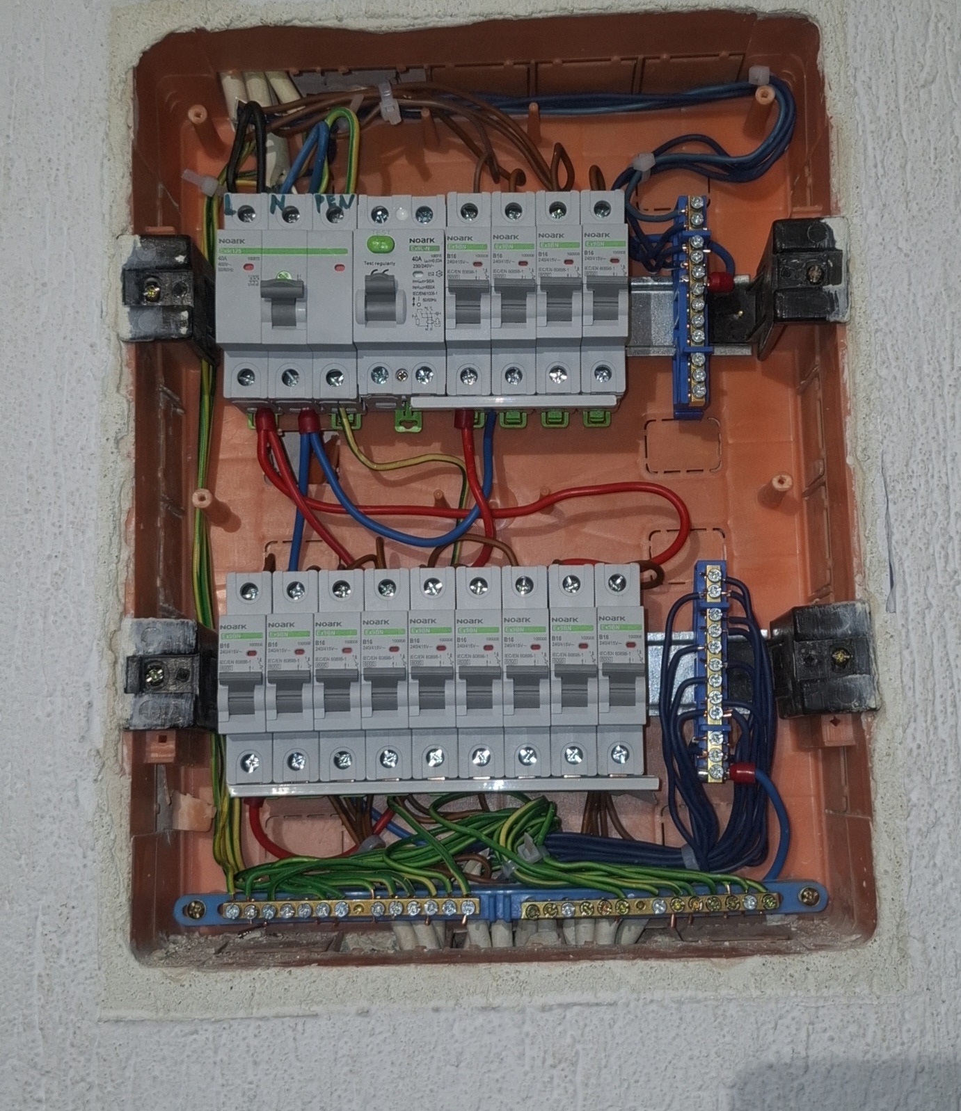 Rozdzielnia elektryczna w brązowej obudowie, z zamontowanymi bezpiecznikami i okablowaniem. Widoczne złącza i przewody w różnych kolorach.