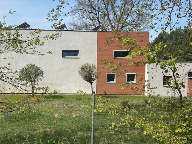 Nowoczesny dom z panelami słonecznymi na dachu, elewacja w dwóch odcieniach, numer domu '50'. Wiosenne drzewa w pierwszym planie.