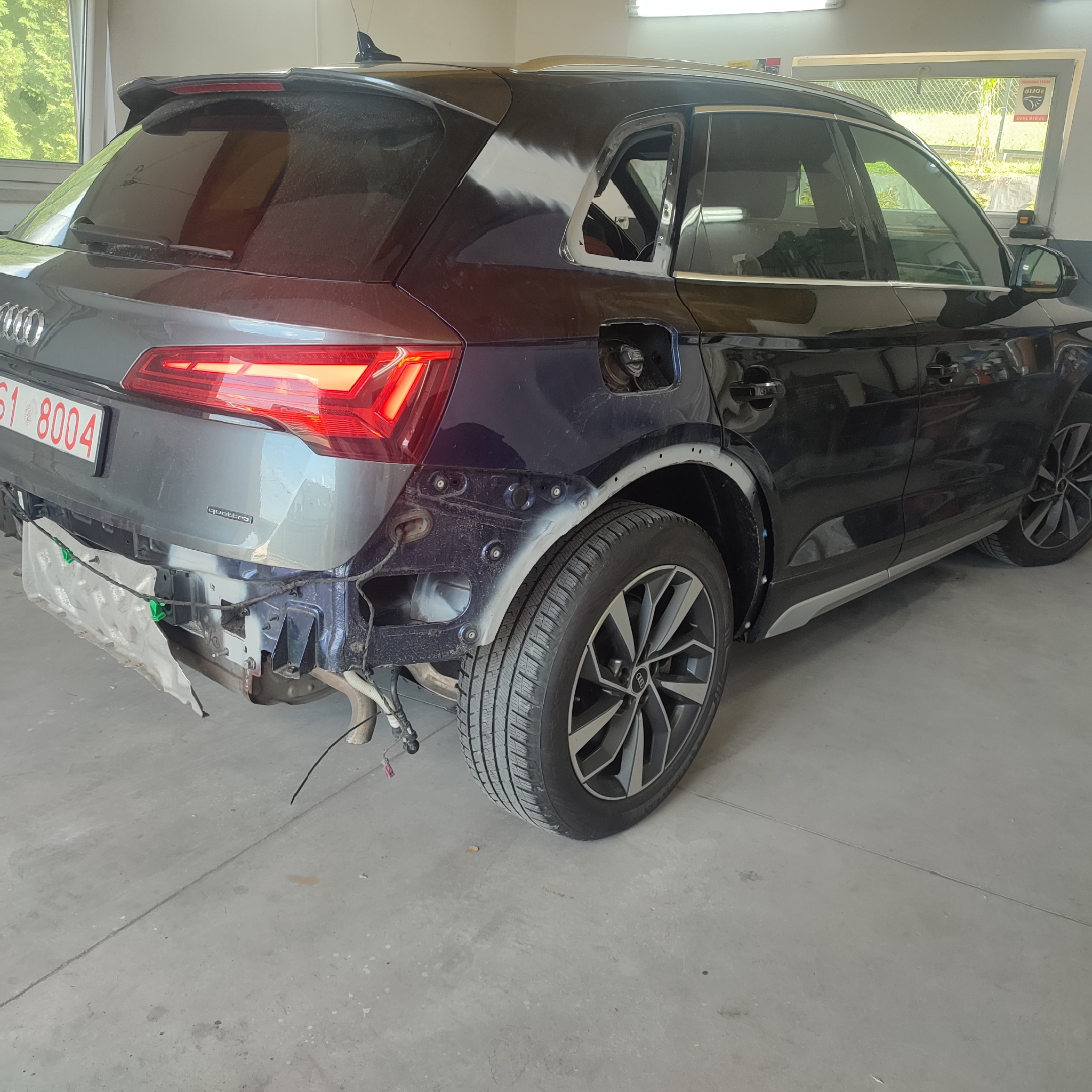 Audi Q5 z uszkodzonym tyłem, w trakcie naprawy w warsztacie, widoczne elementy karoserii przygotowane do lakierowania, brakujące fragmenty zderzaka i błotnika.