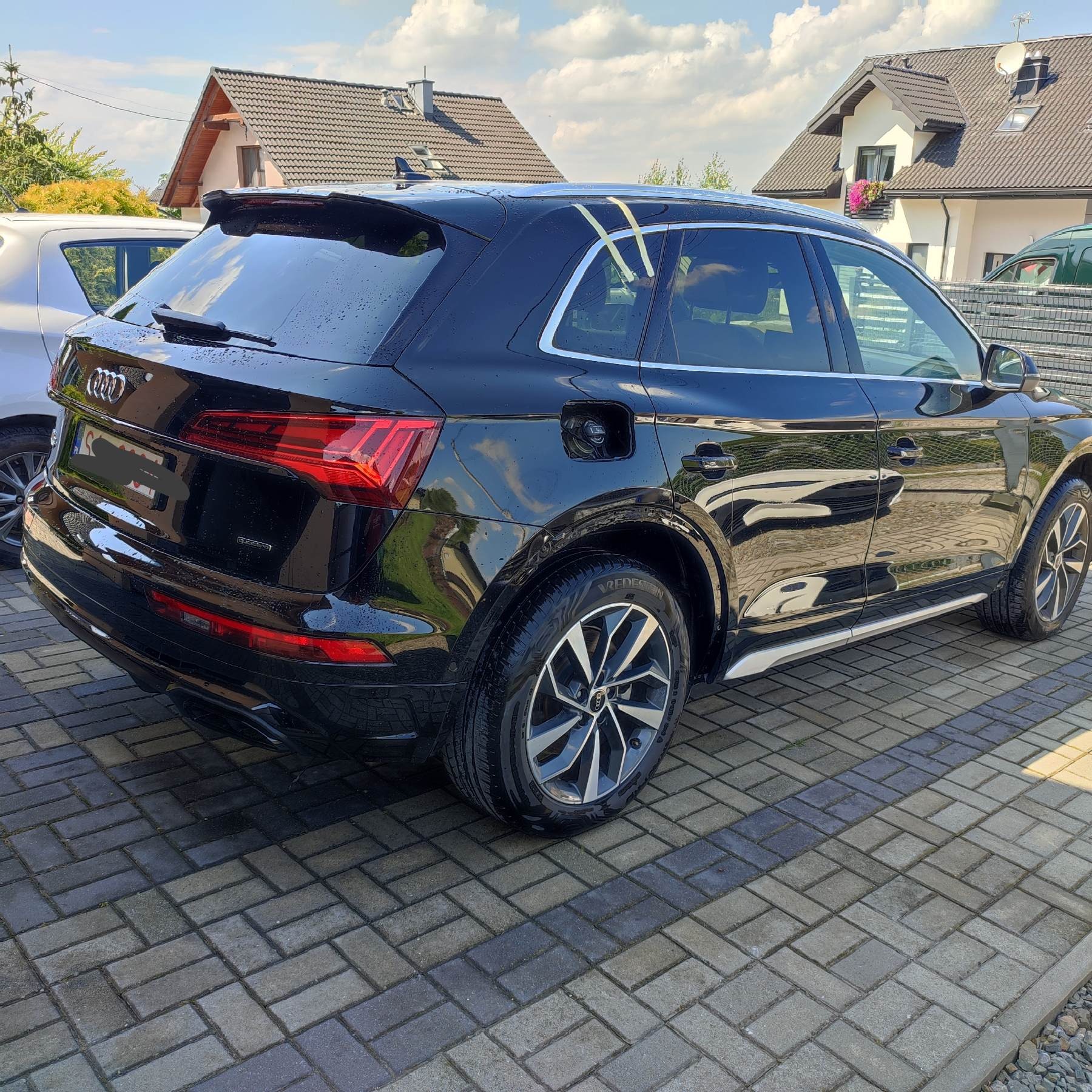 Czarny SUV Audi Q5 po myciu, widoczne ślady wody na karoserii, z otwartym wlewem paliwa, zaparkowany na kostce brukowej przed domem.