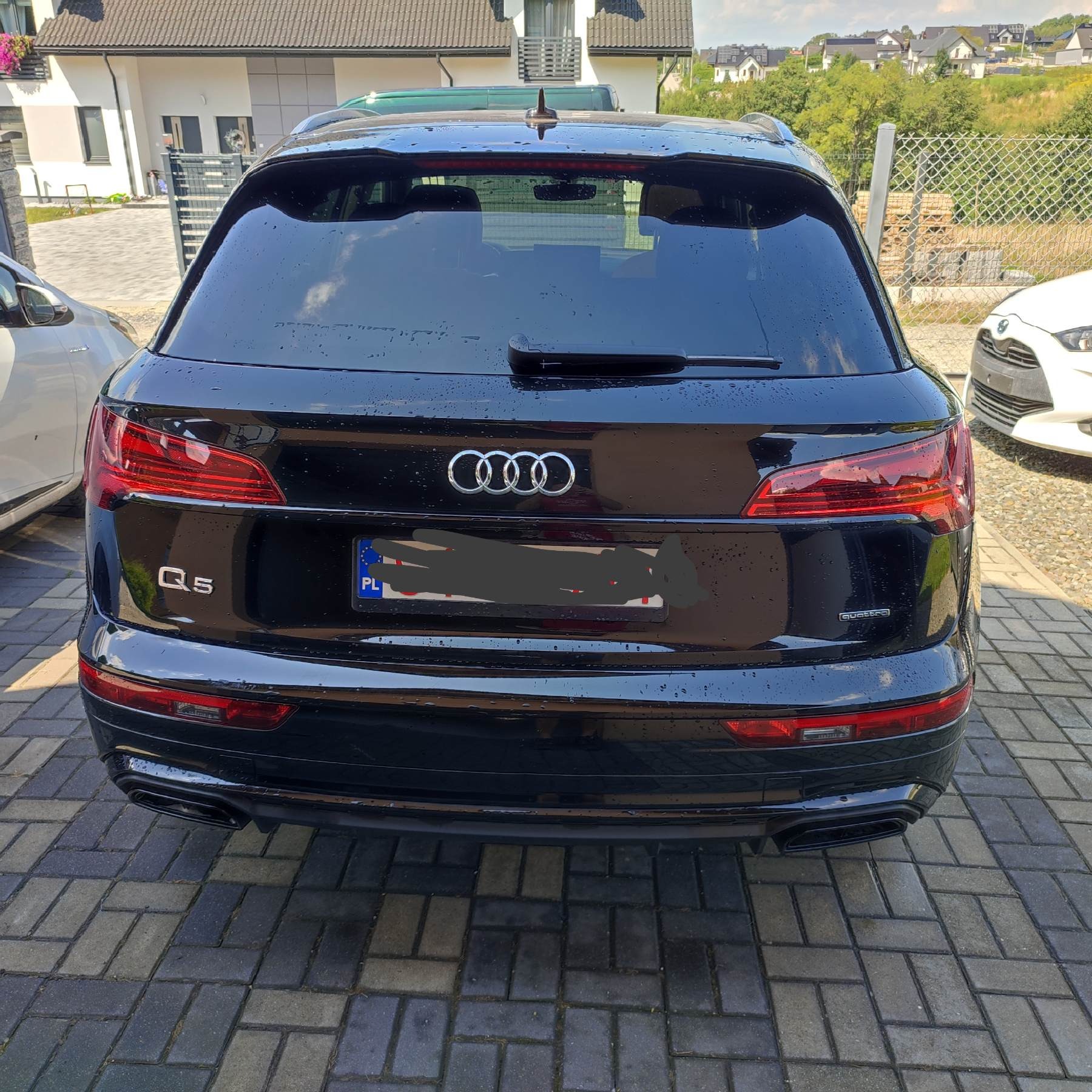Czarny SUV Audi Q5, widok z tyłu, po umyciu, z widocznymi kroplami wody na karoserii, zaparkowany na kostce brukowej.