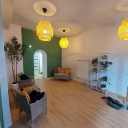 Jasne wnętrze po remoncie: drewniana podłoga, zielona ściana z łukiem, rattanowe meble i lampy. Nowoczesny design z roślinami doniczkowymi.