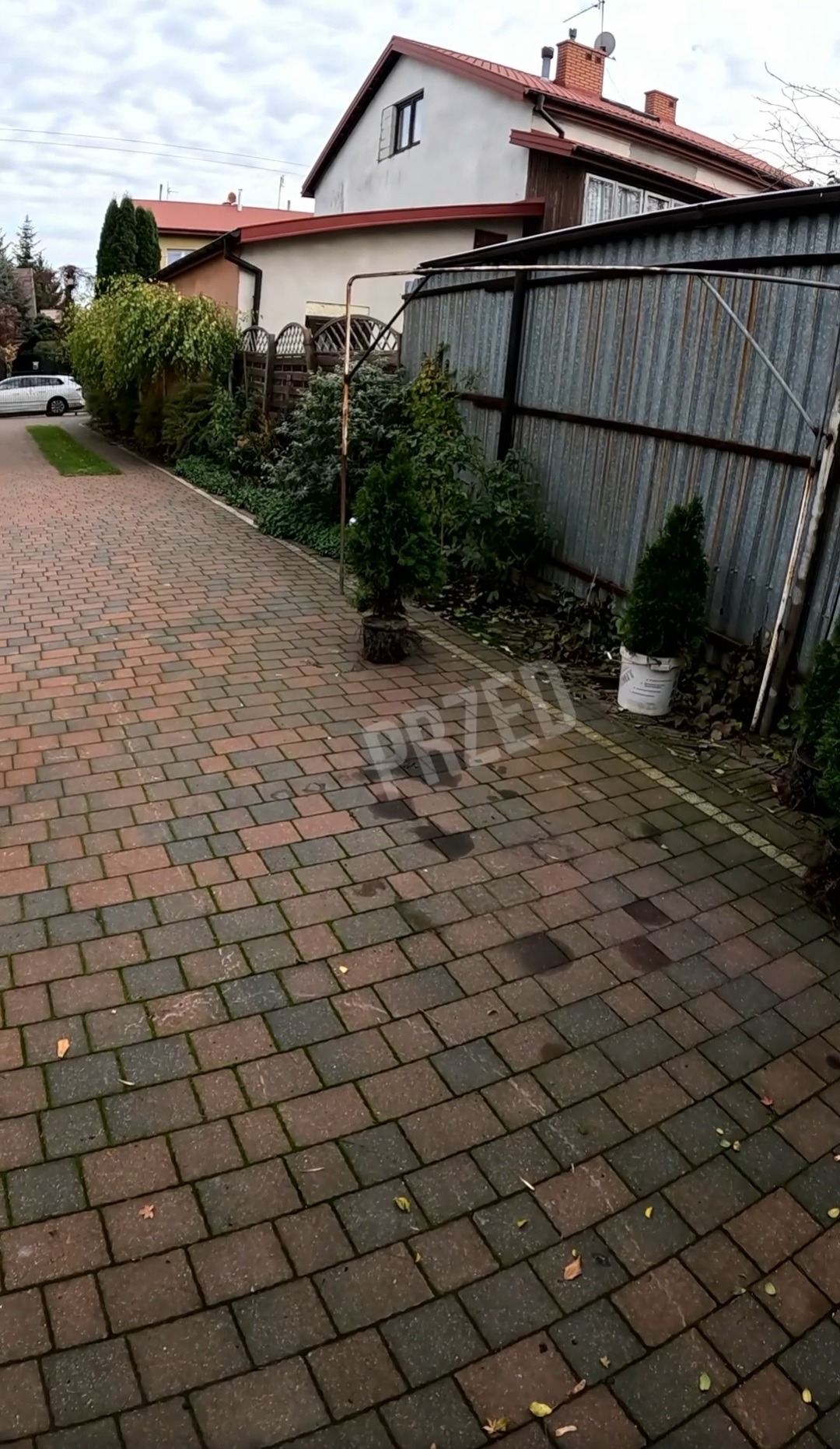 Ceglana kostka brukowa z widocznym napisem 'PRZED', sugerująca etap przed czyszczeniem. W tle budynek mieszkalny i metalowe ogrodzenie.
