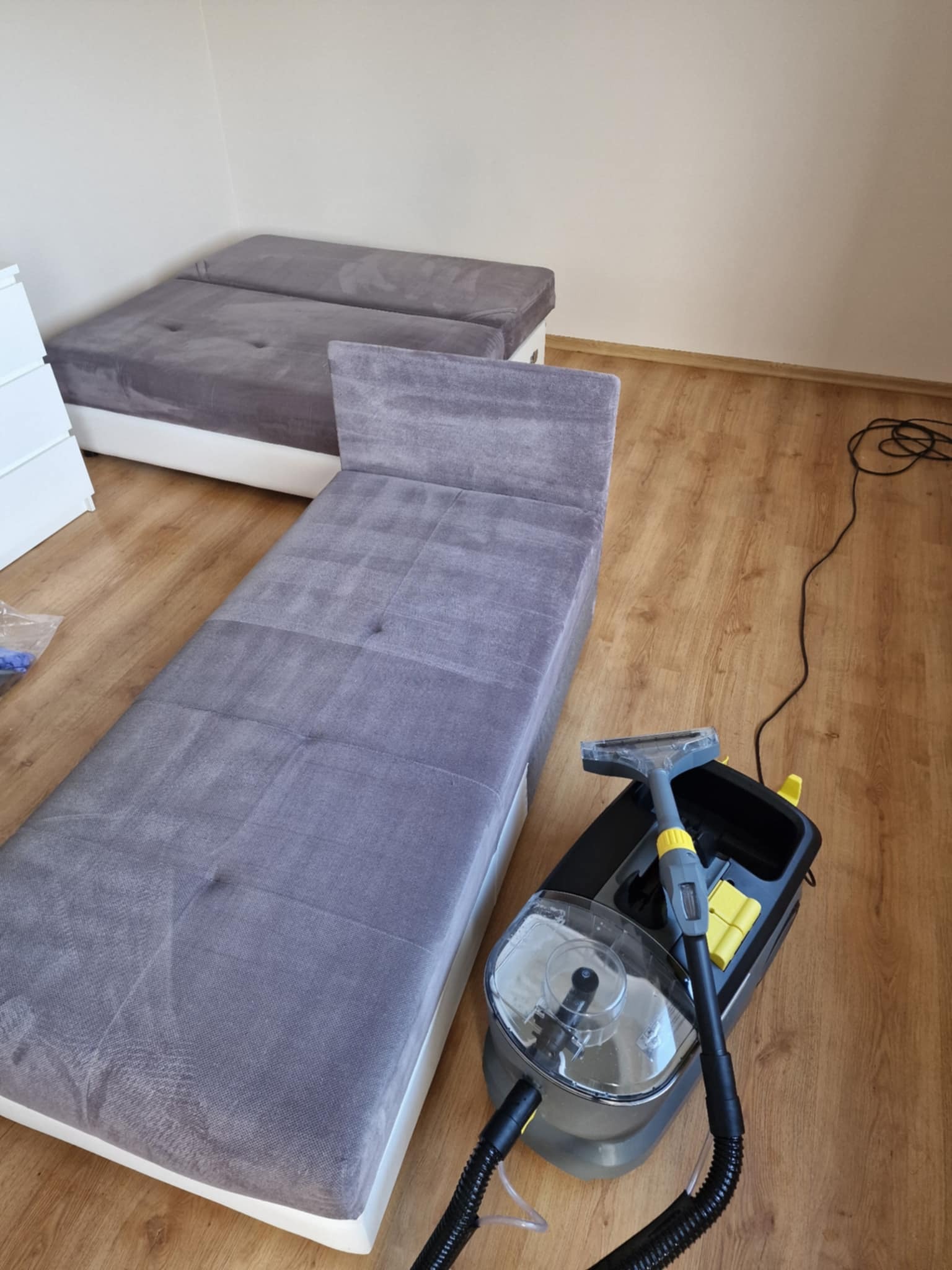Szara sofa modułowa z widocznymi śladami czyszczenia oraz odkurzacz piorący na drewnianej podłodze.