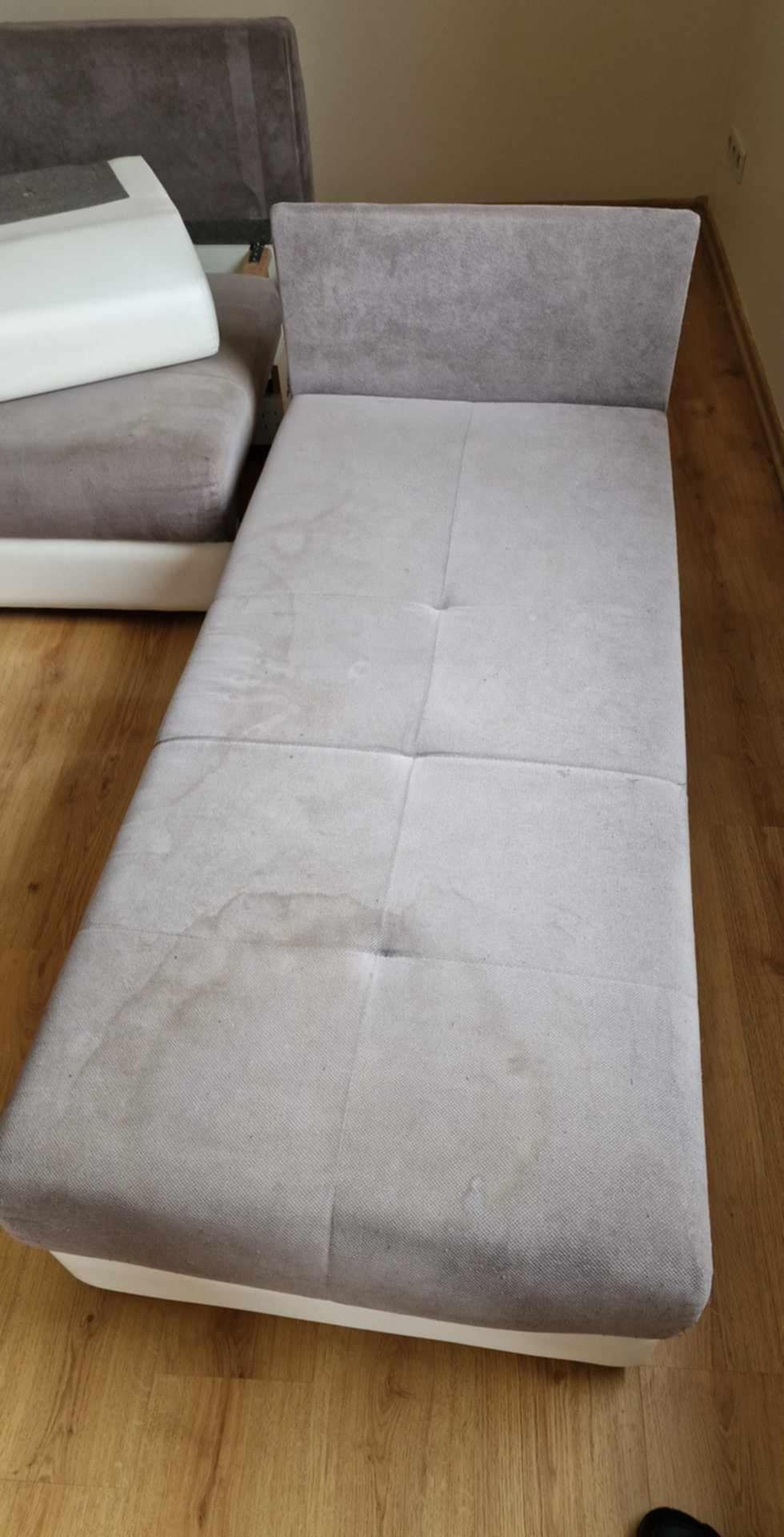 Szara kanapa modułowa z widocznymi plamami na tapicerce, stojąca na panelach podłogowych.