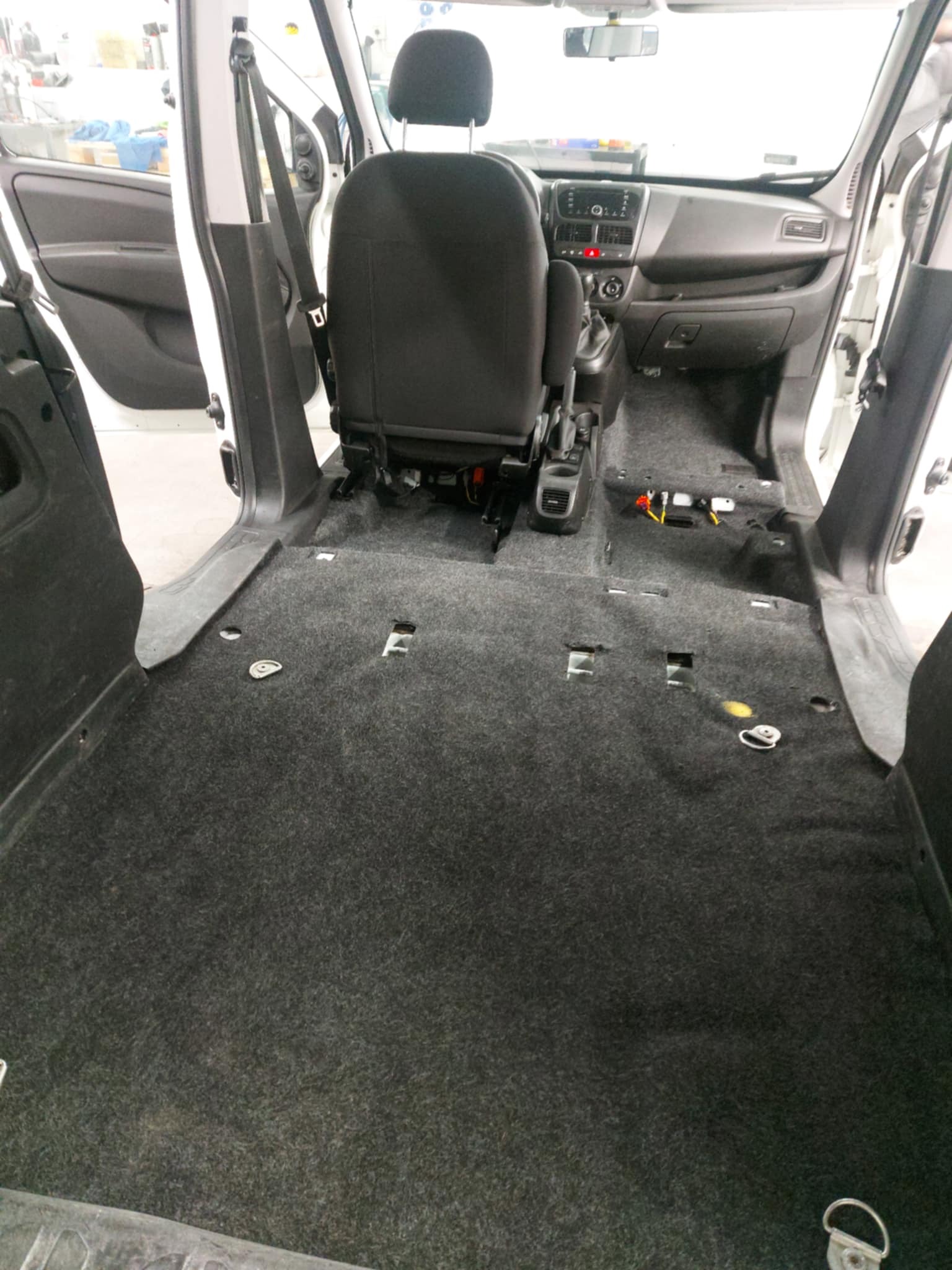 Wnętrze samochodu dostawczego z częściowo zdemontowaną tapicerką podłogową, widoczne otwory montażowe i elementy instalacji elektrycznej.