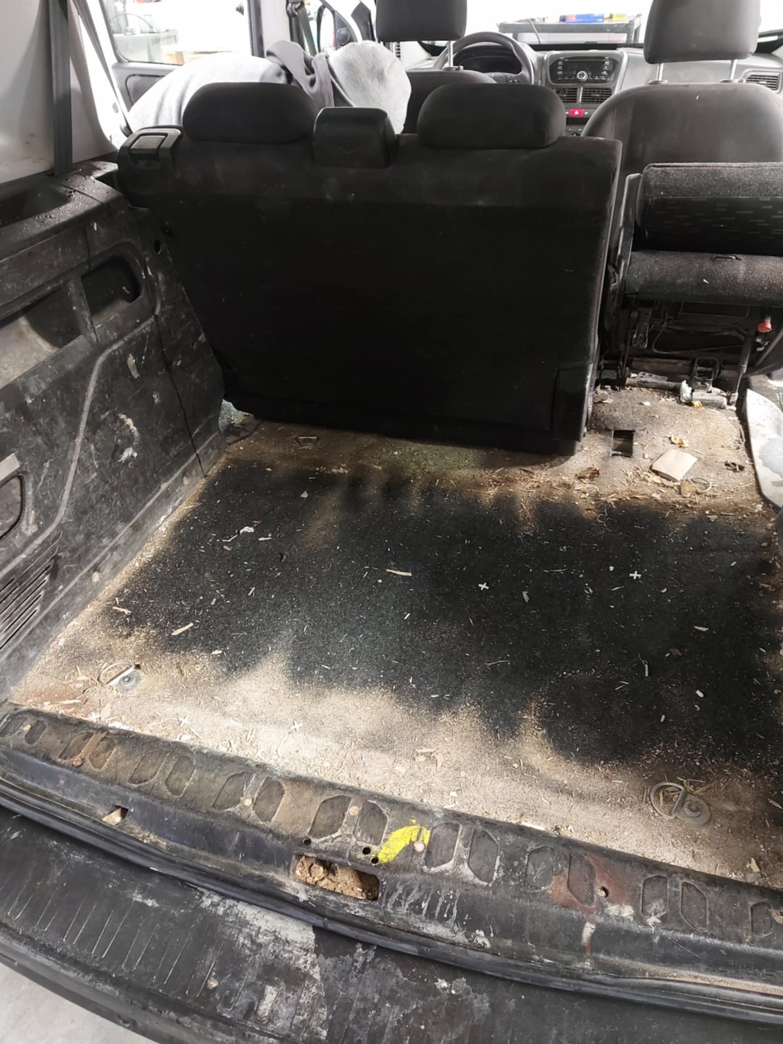 Brudny bagażnik samochodu z widocznymi resztkami piasku, kurzu i drobnymi elementami po remoncie lub budowie, przed czyszczeniem.