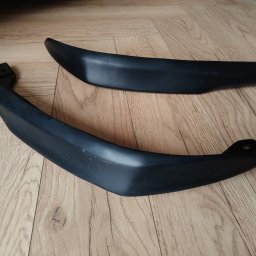 B3Ddesign.pl - Dwa czarne, matowe elementy z tworzywa sztucznego o zakrzywionym kształcie, leżące na panelach podłogowych. Jeden element z widocznym otworem montażowym.