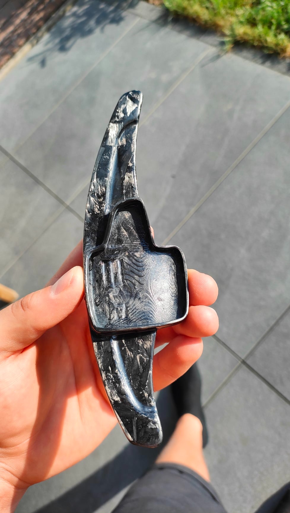 Ręcznie trzymana manetka zmiany biegów z włókna węglowego o unikalnym wzorze, prawdopodobnie do Forda Focus MK III, sfotografowana na zewnątrz w słoneczny dzień.