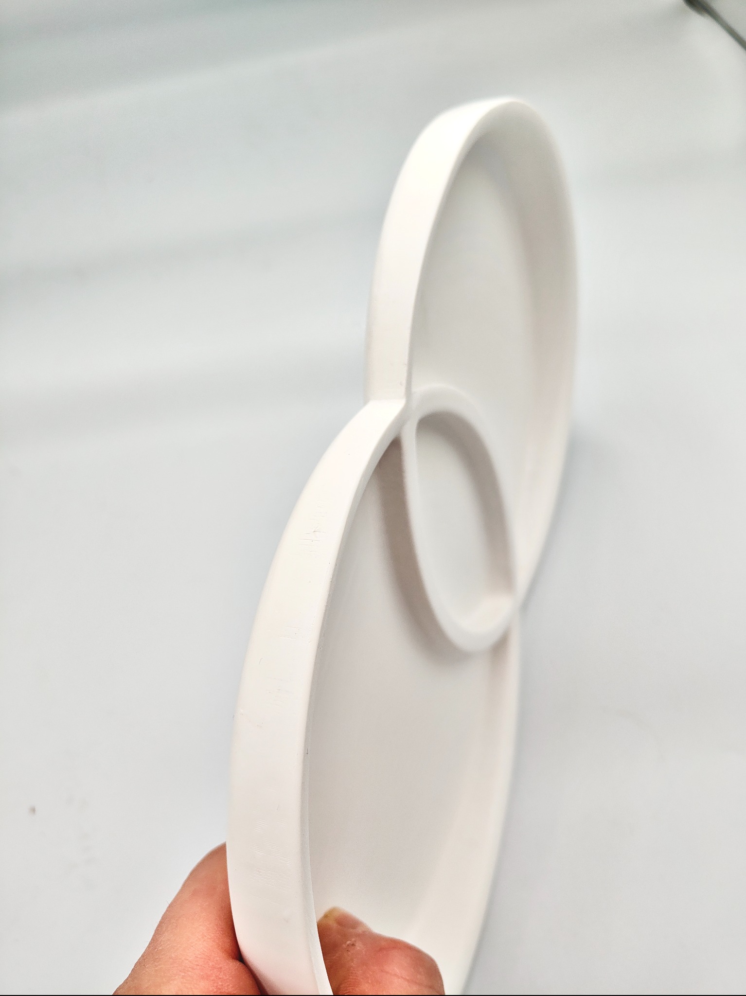 Biały, trójdzielny talerz z tworzywa sztucznego, wydrukowany w 3D, trzymany w dłoni na jasnym tle. Widoczne delikatne warstwy druku.