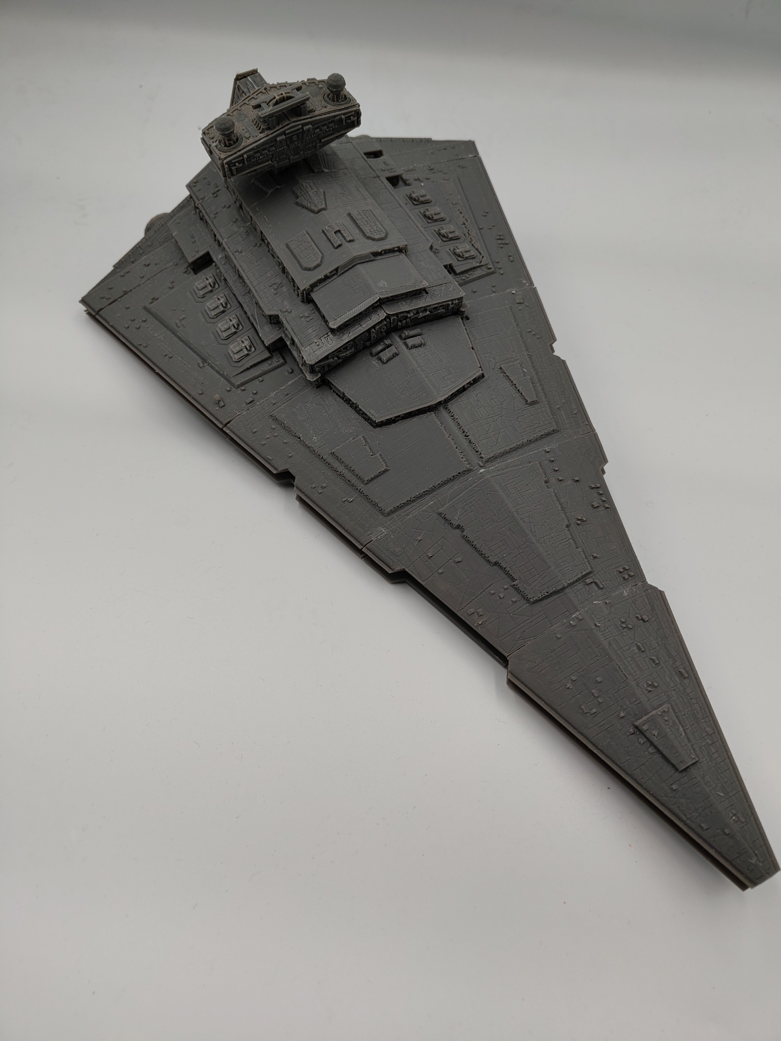 Szary model Star Destroyer z Gwiezdnych Wojen, wydrukowany w 3D, z widocznymi detalami i teksturą druku, leżący na jasnym tle. Model statku kosmicznego.