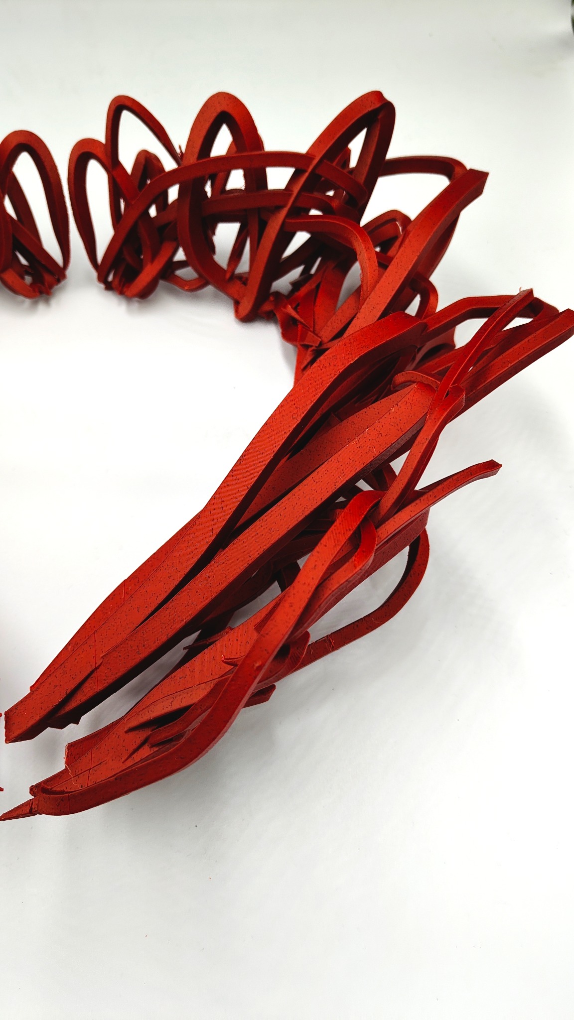 Czerwony, abstrakcyjny model z pasków tworzy dynamiczną kompozycję na białym tle. Widoczne ślady warstw, sugerujące technikę wytwarzania addytywnego.