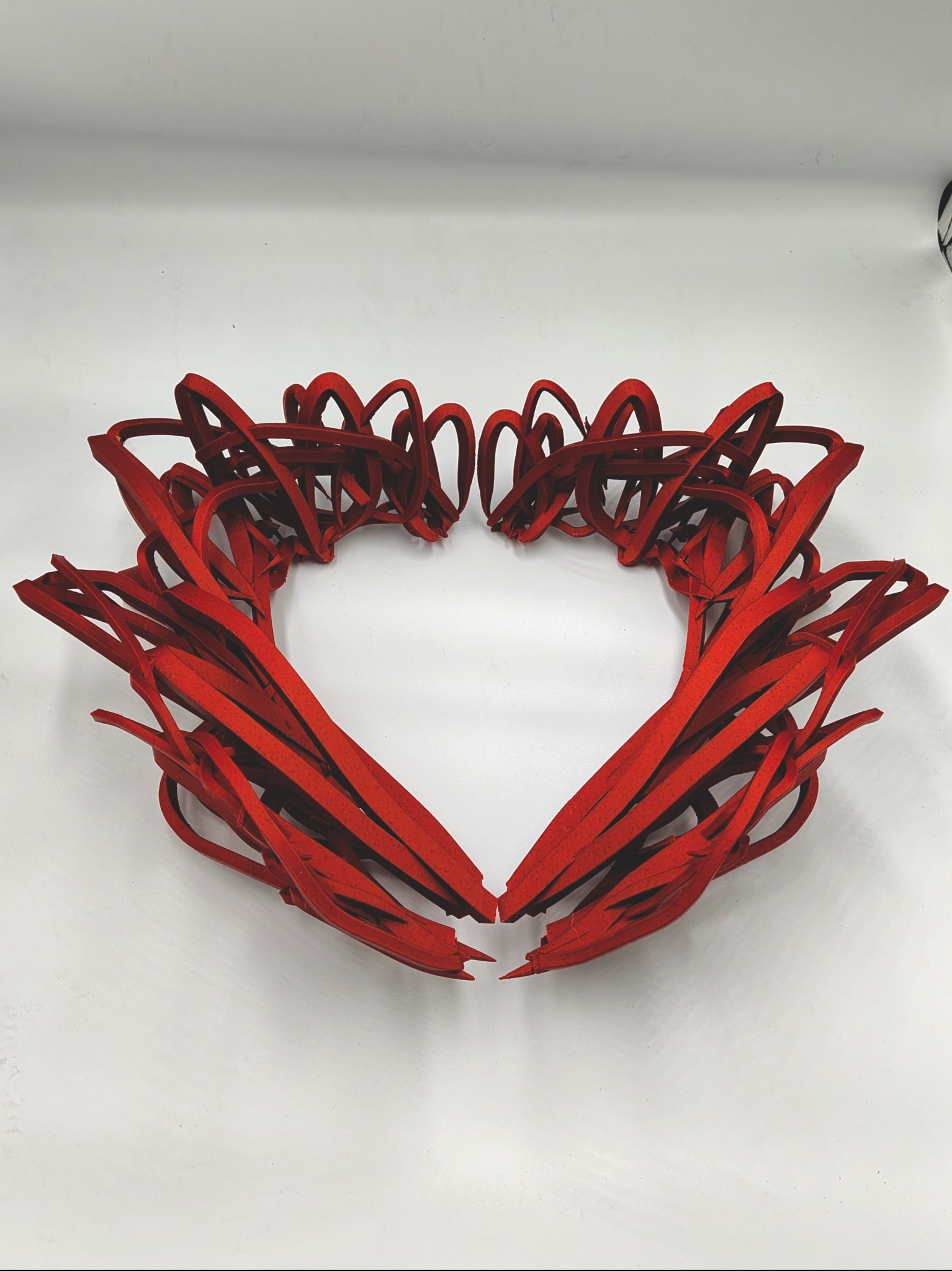 Czerwony, abstrakcyjny kształt serca z wydrukowanych elementów na białym tle. Unikalna kompozycja z precyzyjnie ułożonych, zakrzywionych form.