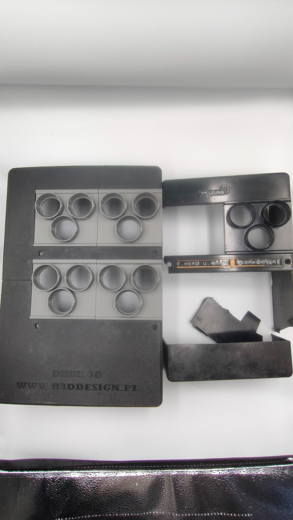 Elementy obudowy, prawdopodobnie do urządzenia grzewczego, wykonane metodą druku 3D. Widoczne otwory i napisy. Część elementów jest uszkodzona.