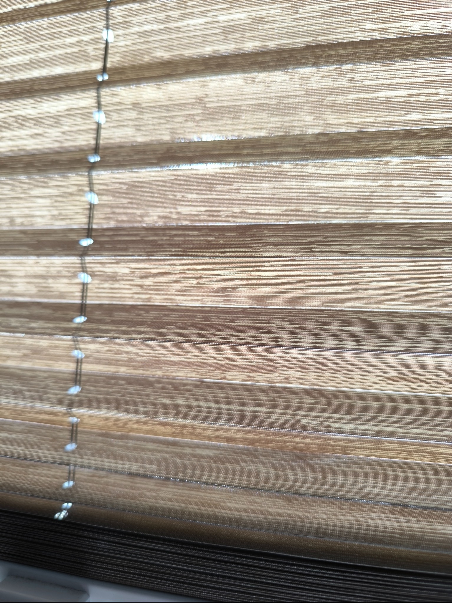 Beżowe plisy okienne z delikatnym wzorem i sznurkiem sterującym, widoczne z bliska, z wyraźną fakturą materiału.