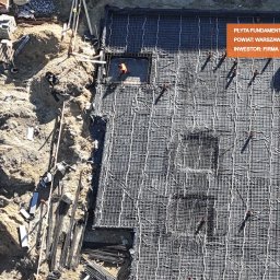 Czaporowski Żurawski sp. z o.o. - Z góry widoczna płyta fundamentowa zbrojona siatką stalową, przygotowana do wylania betonu na budowie wielorodzinnej w powiecie warszawskim zachodnim; pracownik w pomarańczowej kamizelce w wykopie.