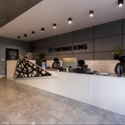 Nowoczesne biuro z recepcją, logo Thermo King na ścianie, szara podłoga i oświetlenie punktowe.