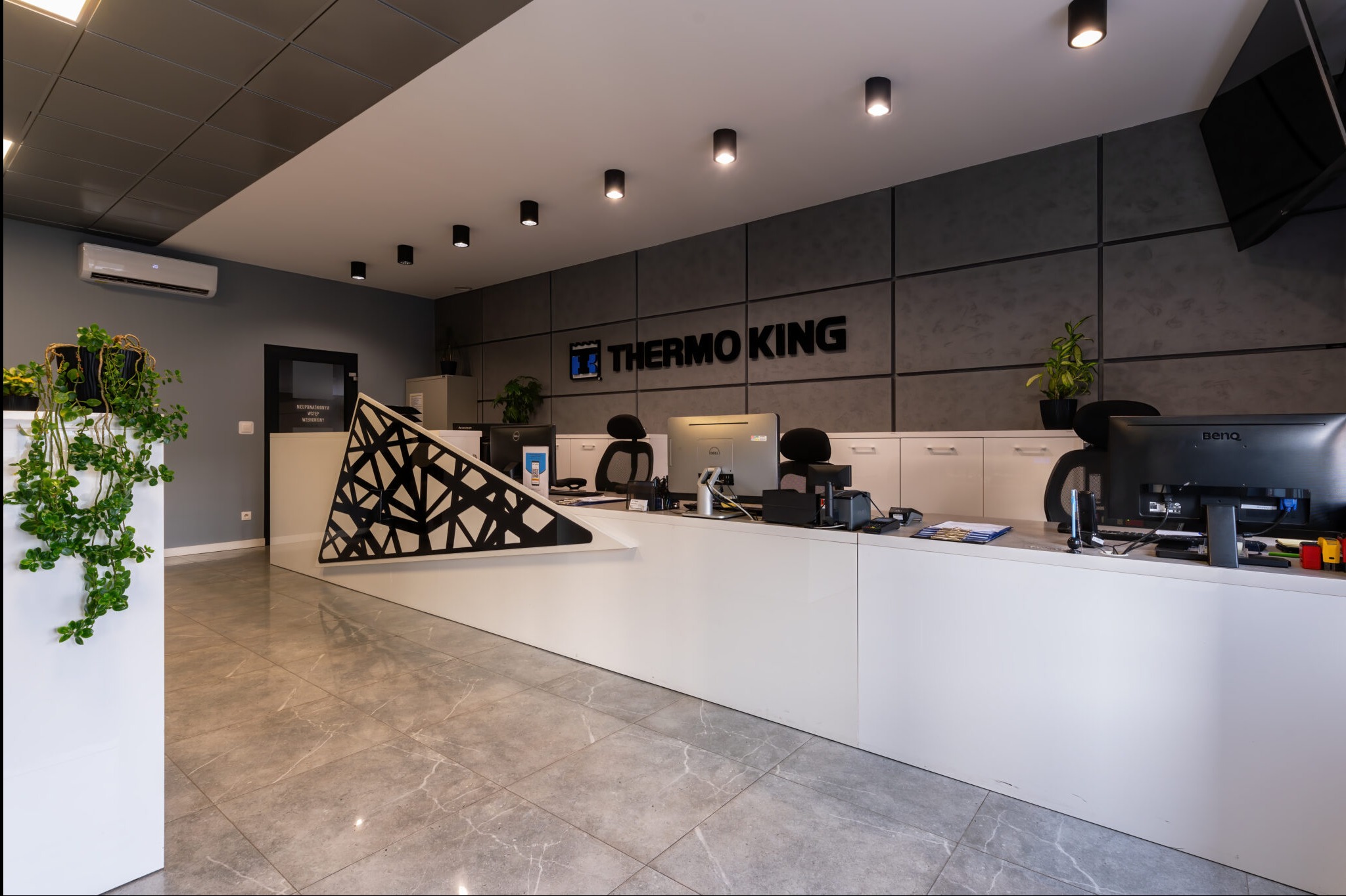 Nowoczesne biuro z recepcją, logo Thermo King na ścianie, szara podłoga i oświetlenie punktowe.