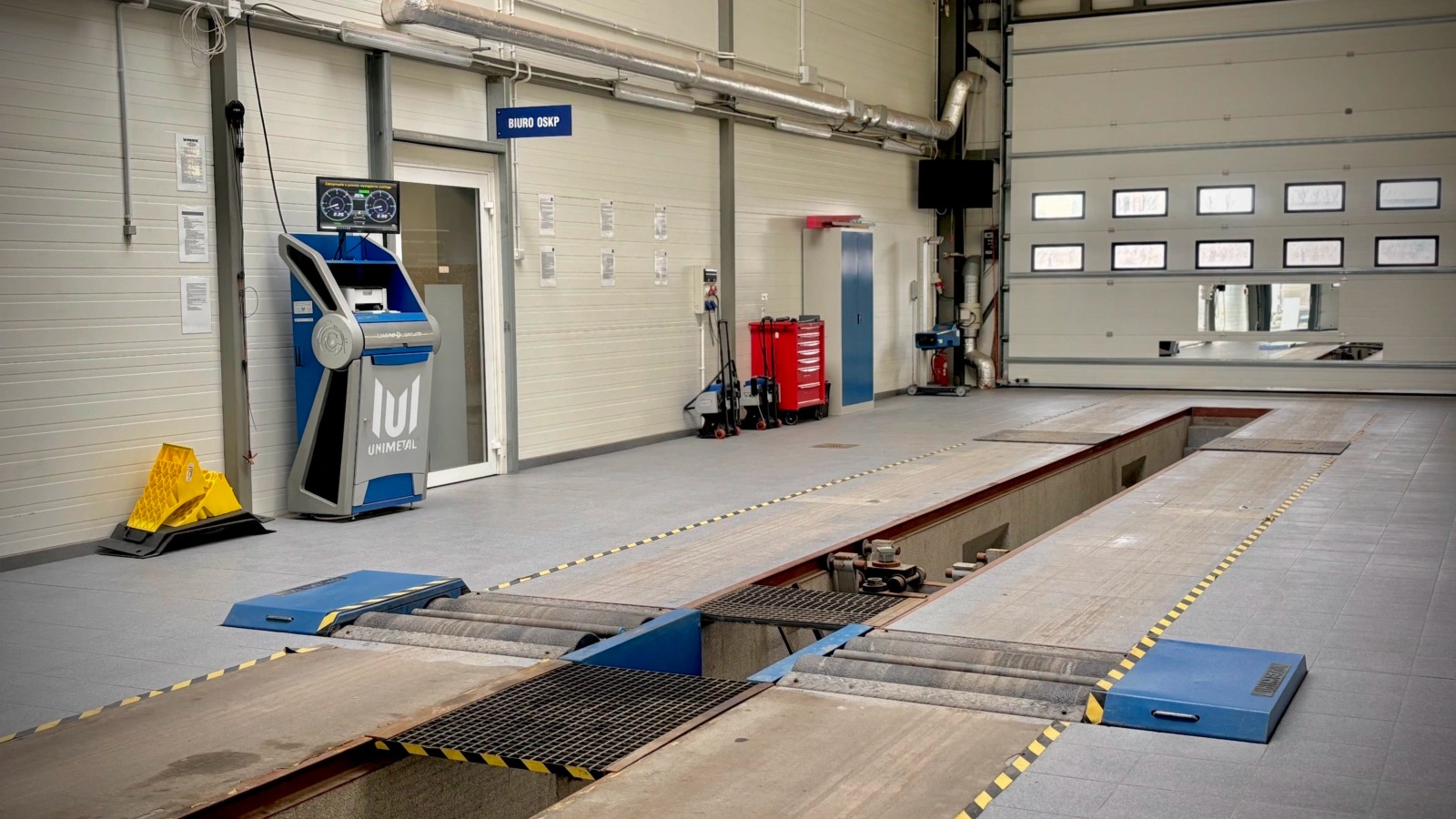 Stanowisko diagnostyczne z kanałem w warsztacie, widoczny analizator spalin Unimetal, narzędzia i brama garażowa.