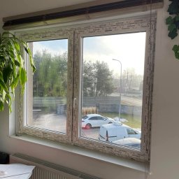 KPM Patrycja Centner - Nowe okno PCV z roletami wewnętrznymi, widok na podjazd z samochodami i drzewa w tle.