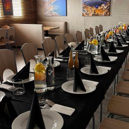 Restauracja Veneto - Elegancko nakryty stół z czarnym obrusem, białymi talerzami i czarnymi serwetkami, szklanki i dzbanki z wodą i cytryną. Gotowy na przyjęcie.