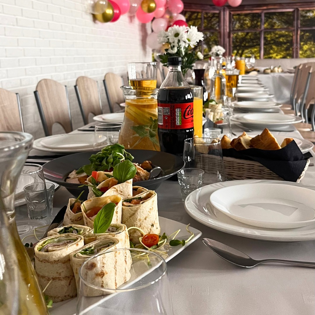 Uroczysty stół z wrapami, sałatką i napojami. W tle dekoracje balonowe i okno. Idealne na przyjęcie okolicznościowe lub firmowy event. Elegancki catering.
