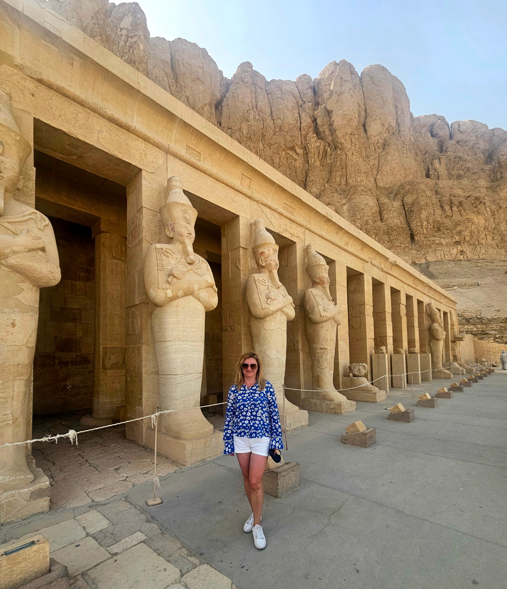 Turystka w kolorowej bluzce pozuje na tle starożytnej świątyni z rzeźbami faraonów i skalistych gór w Dolinie Królów w Egipcie. Słoneczny dzień.