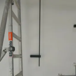 Montaż czarnej lampy ściennej na białej ścianie, widoczne rusztowanie, przygotowane schody, etap prac wykończeniowych.