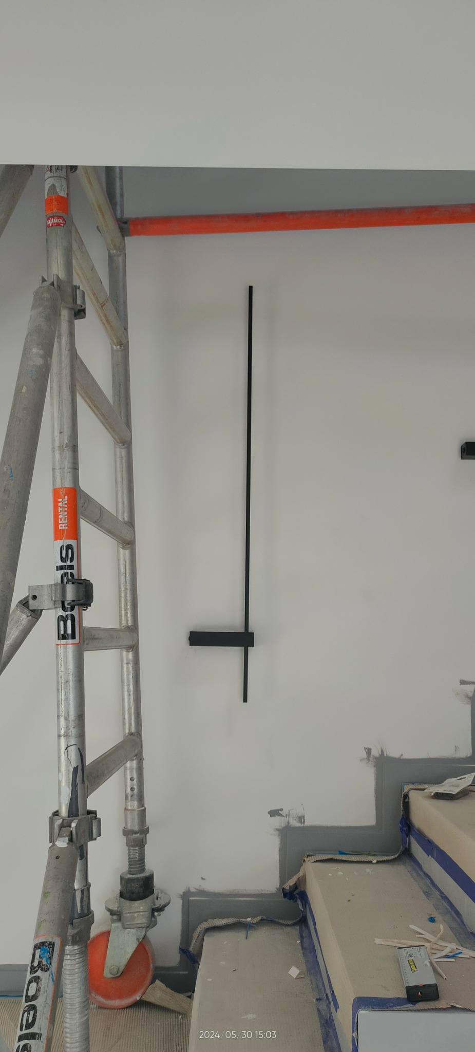 Montaż czarnej lampy ściennej na białej ścianie, widoczne rusztowanie, przygotowane schody, etap prac wykończeniowych.