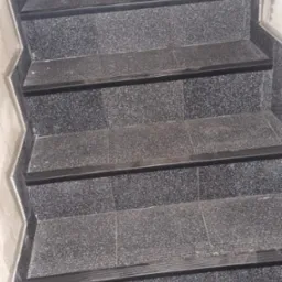 Schody wyłożone ciemną, szarą terakotą z czarnymi listwami antypoślizgowymi na krawędziach stopni, widoczne ślady zaprawy na ścianach.