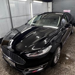 Autoart - Błyszczący, czarny Ford Mondeo po umyciu, zaparkowany w myjni z widoczną tablicą rejestracyjną.
