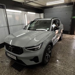 Autoart - Szary samochód Volvo XC40 po umyciu, stojący wewnątrz myjni z mokrą podłogą i otwartą bramą garażową w tle.