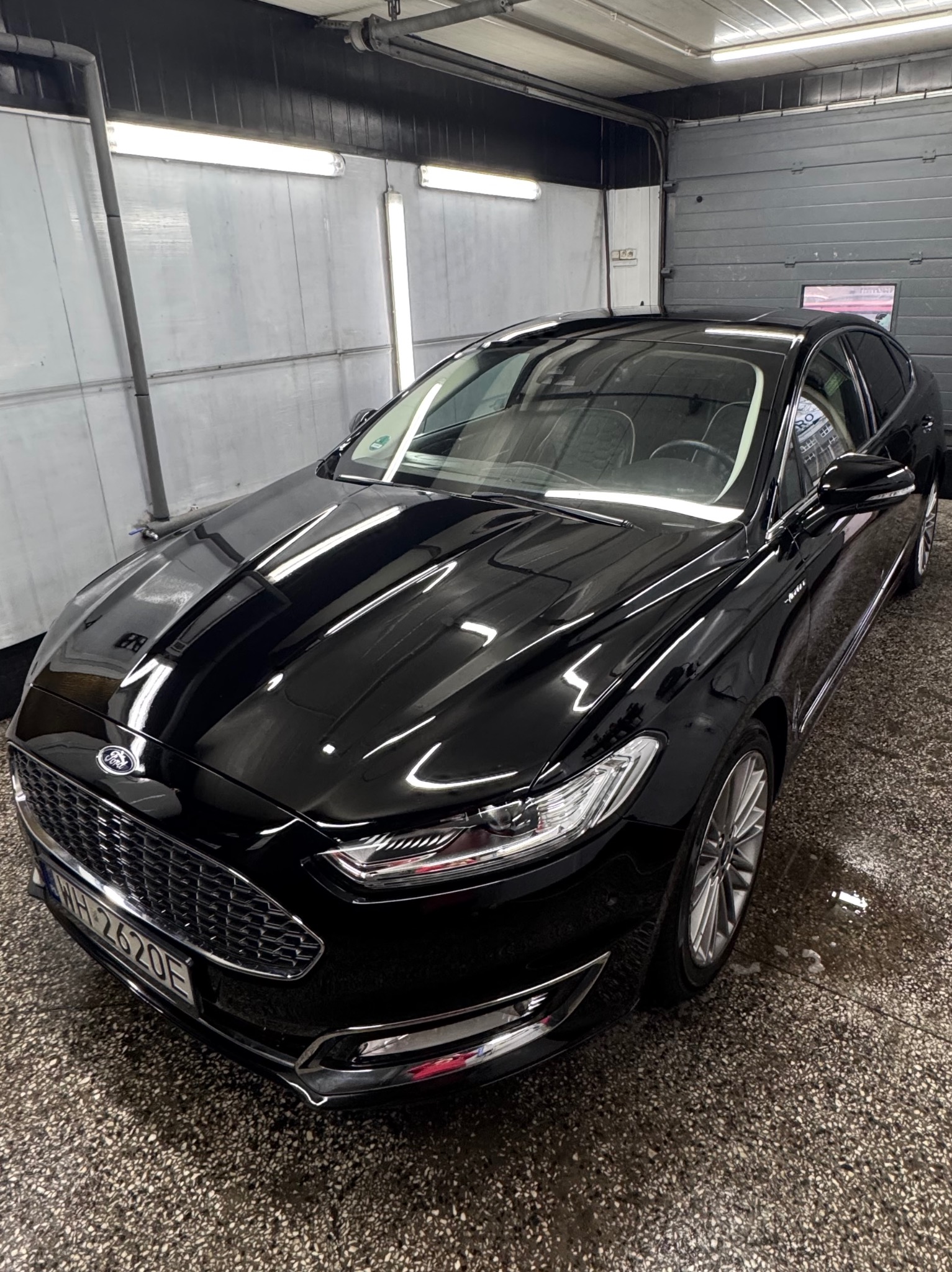 Błyszczący, czarny Ford Mondeo po umyciu, zaparkowany w myjni z widoczną tablicą rejestracyjną.
