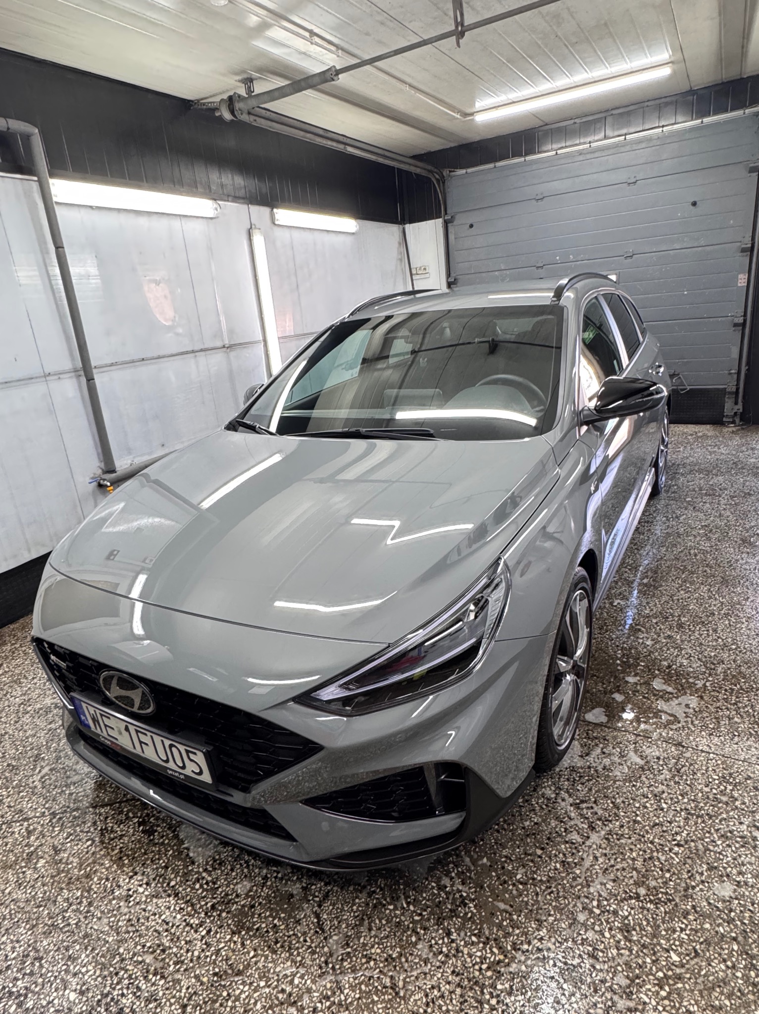 Szary samochód Hyundai i30 kombi po umyciu, z widocznymi kroplami wody na lakierze i mokrej posadzce myjni.