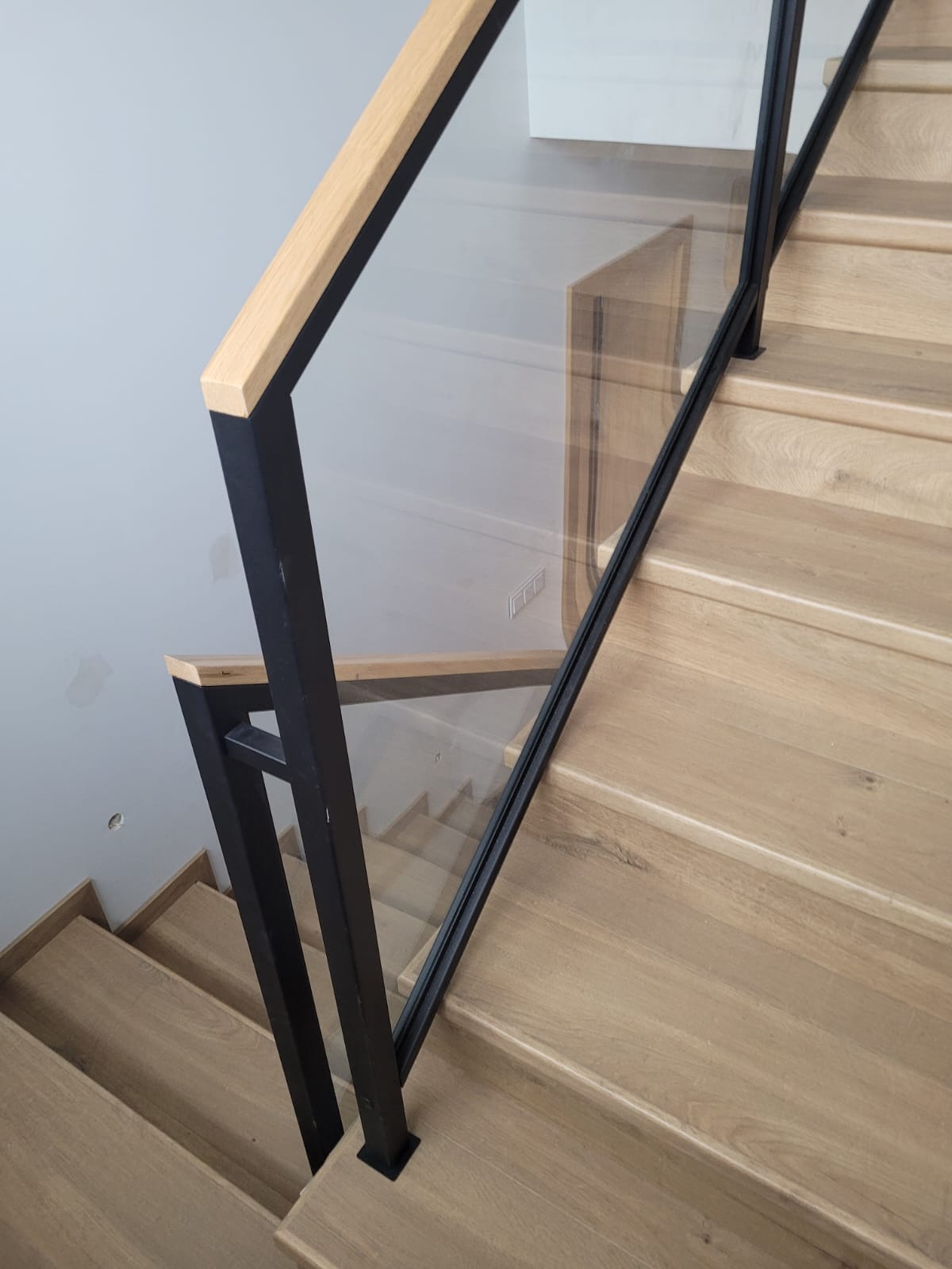 Schody z jasnego drewna z nowoczesną balustradą ze szkła i czarnego metalu, widok z góry, delikatne oświetlenie.