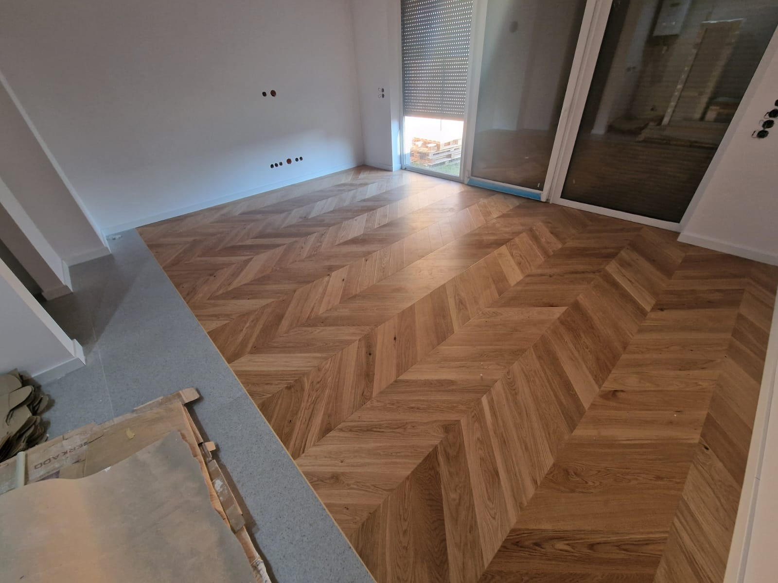 Nowo ułożony parkiet w jodełkę francuską, z widocznymi kartonami po panelach w rogu pomieszczenia i przygotowanymi otworami na gniazdka elektryczne w ścianie.