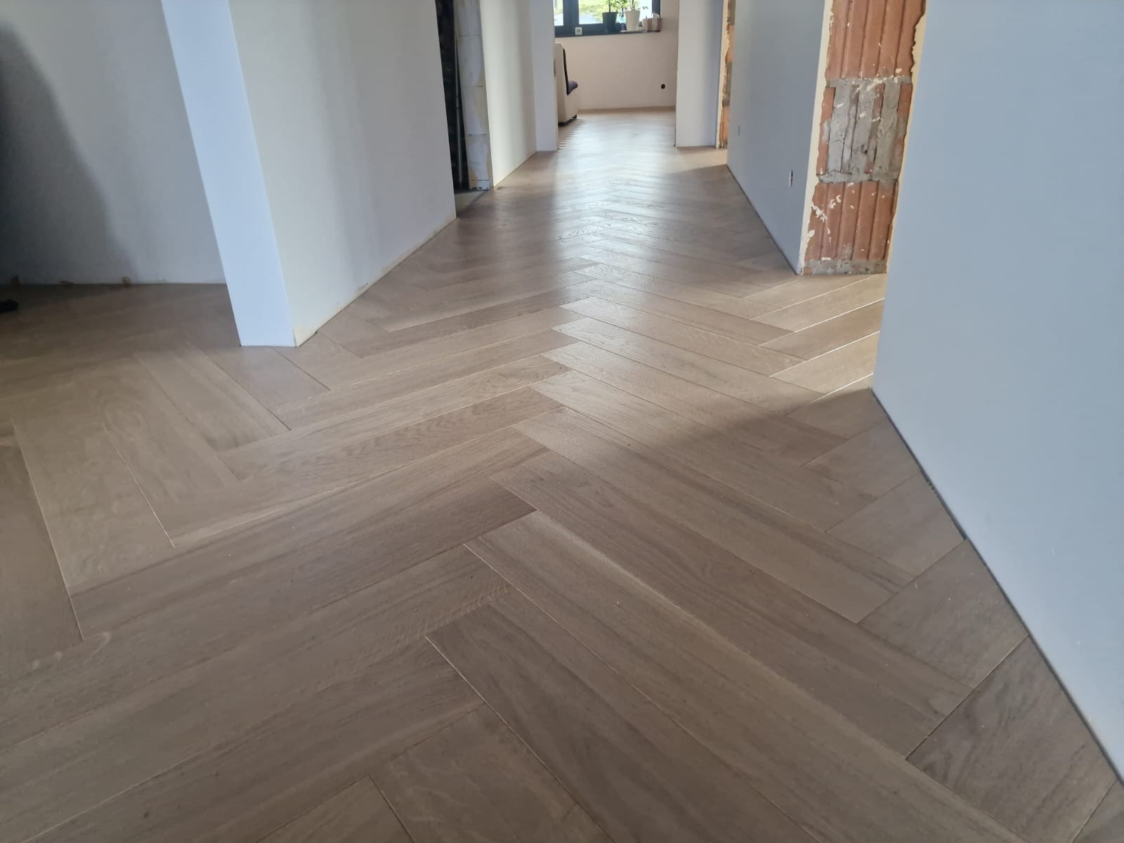 Ułożony parkiet w jodełkę w korytarzu w trakcie remontu, widoczne surowe ściany i przygotowane otwory drzwiowe.