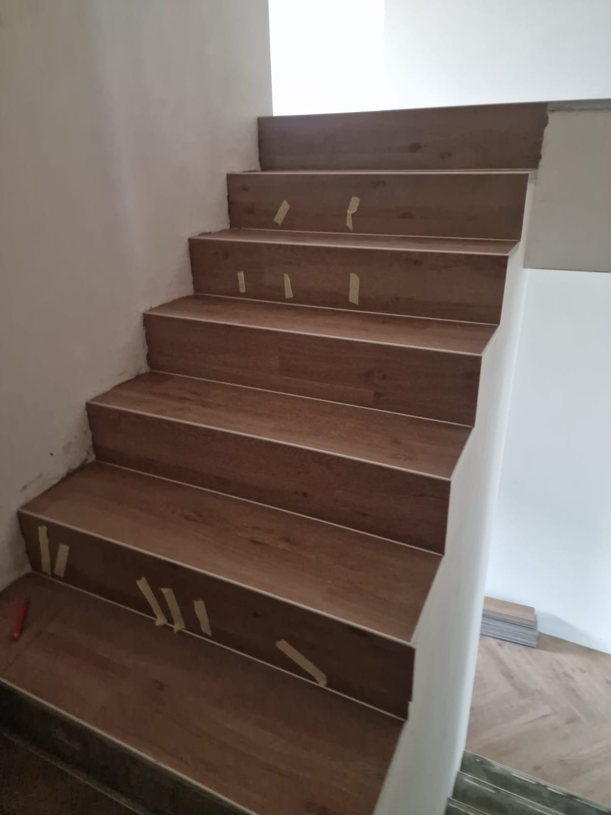 Schody wyłożone panelami imitującymi drewno, zabezpieczone taśmą malarską na czas montażu, widoczne panele podłogowe w tle.