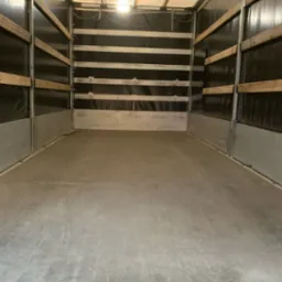 Wnętrze pustej przestrzeni ładunkowej samochodu dostawczego z drewnianymi listwami zabezpieczającymi na ścianach i oświetleniem sufitowym