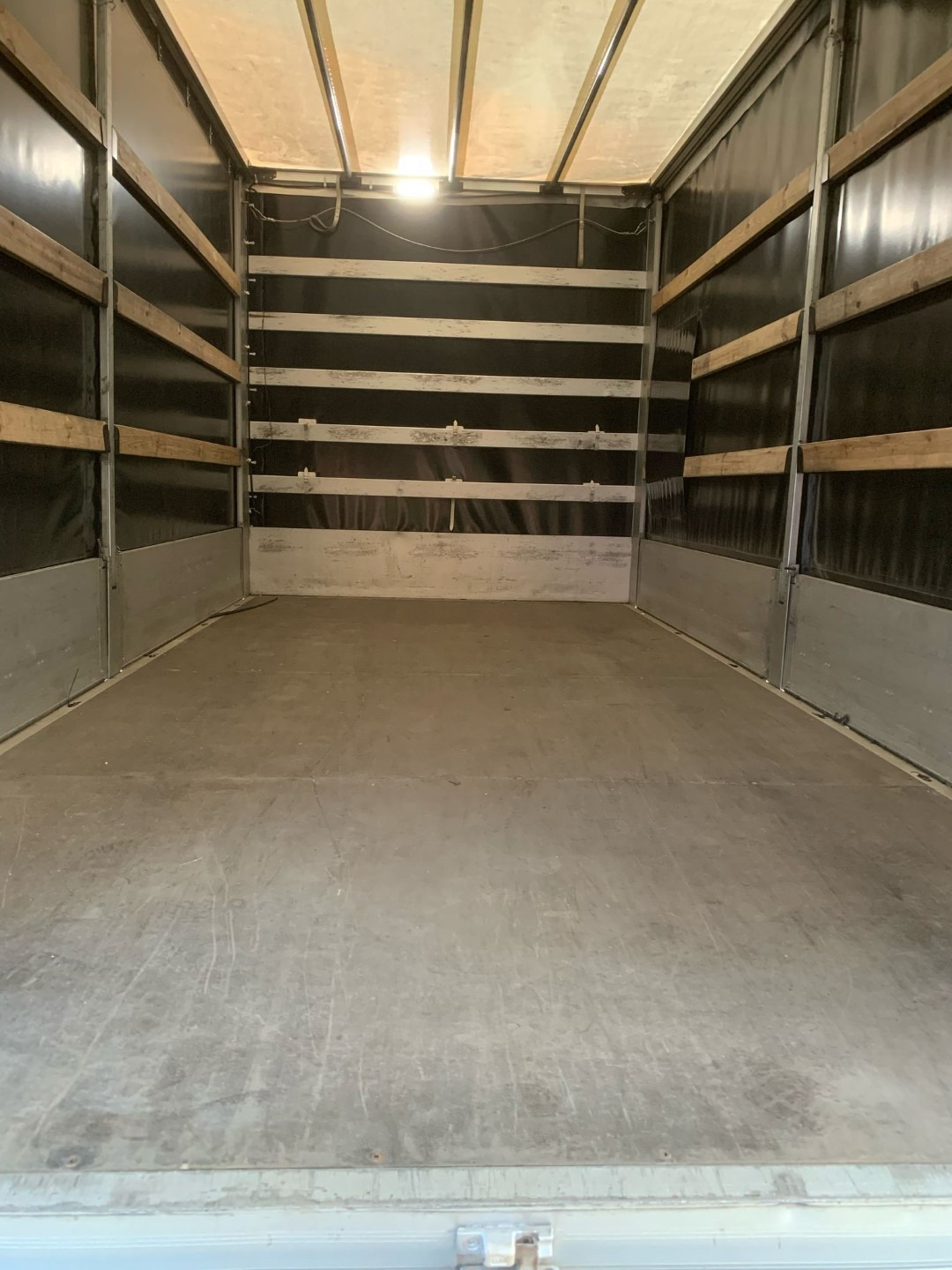 Wnętrze pustej przestrzeni ładunkowej samochodu dostawczego z drewnianymi listwami zabezpieczającymi na ścianach i oświetleniem sufitowym