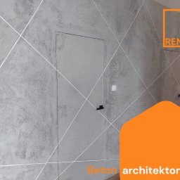 RemFix - Ściana z efektem betonu architektonicznego, dekorowana białymi liniami tworzącymi wzór rombów. Ukryte drzwi z minimalistycznym uchwytem. Widoczny włącznik światła.