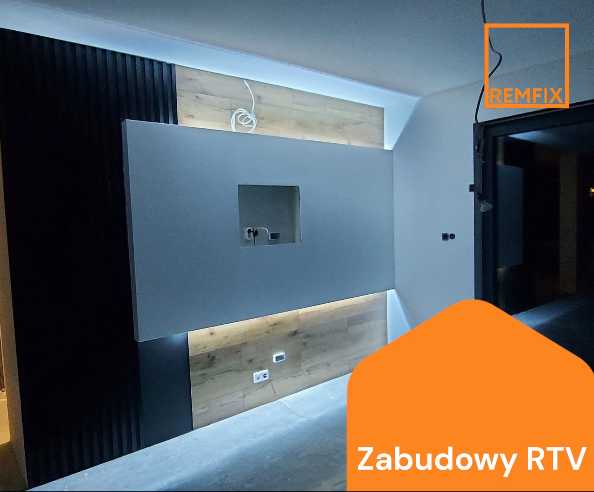 Nowoczesna zabudowa RTV z podświetleniem LED, drewnianymi panelami i szarą ścianką z otworem na telewizor. Widoczne gniazdka elektryczne i kable.