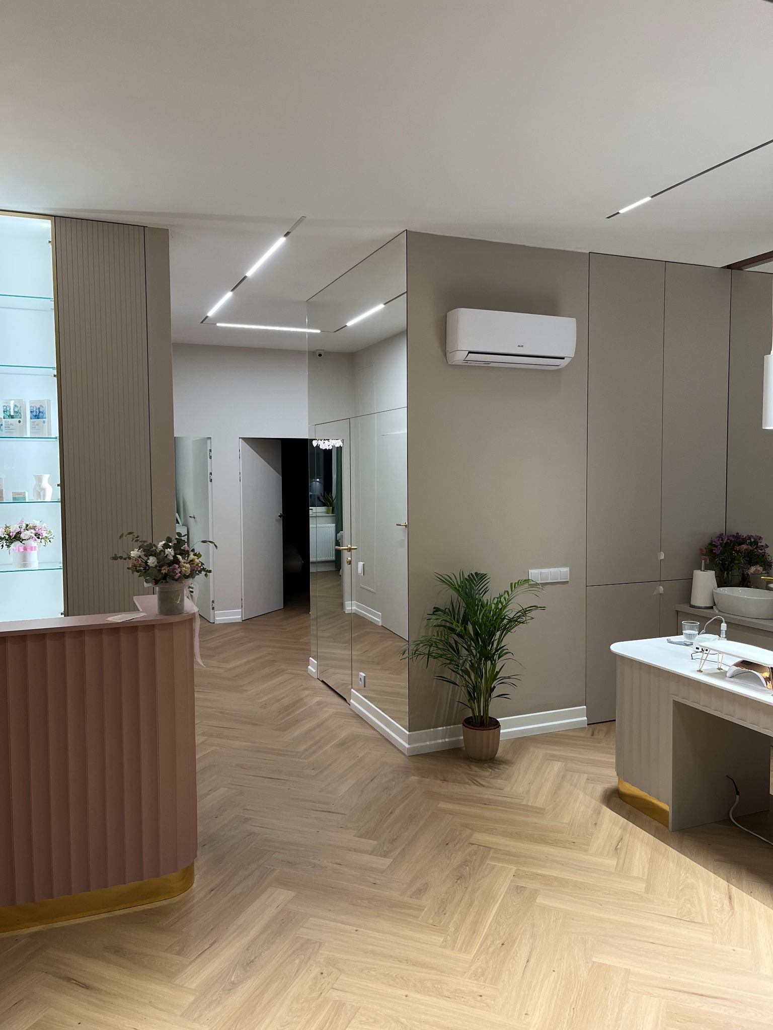 Nowoczesne wnętrze biura z recepcją w odcieniach różu, parkietem w jodełkę, klimatyzacją na ścianie i lustrami powiększającymi przestrzeń.