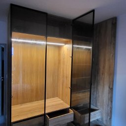 Ex-Mebel Marek Szpak - Nowoczesna szafa wnękowa z drewnianymi frontami, podświetleniem LED i otwartymi szufladami, widok z dołu.