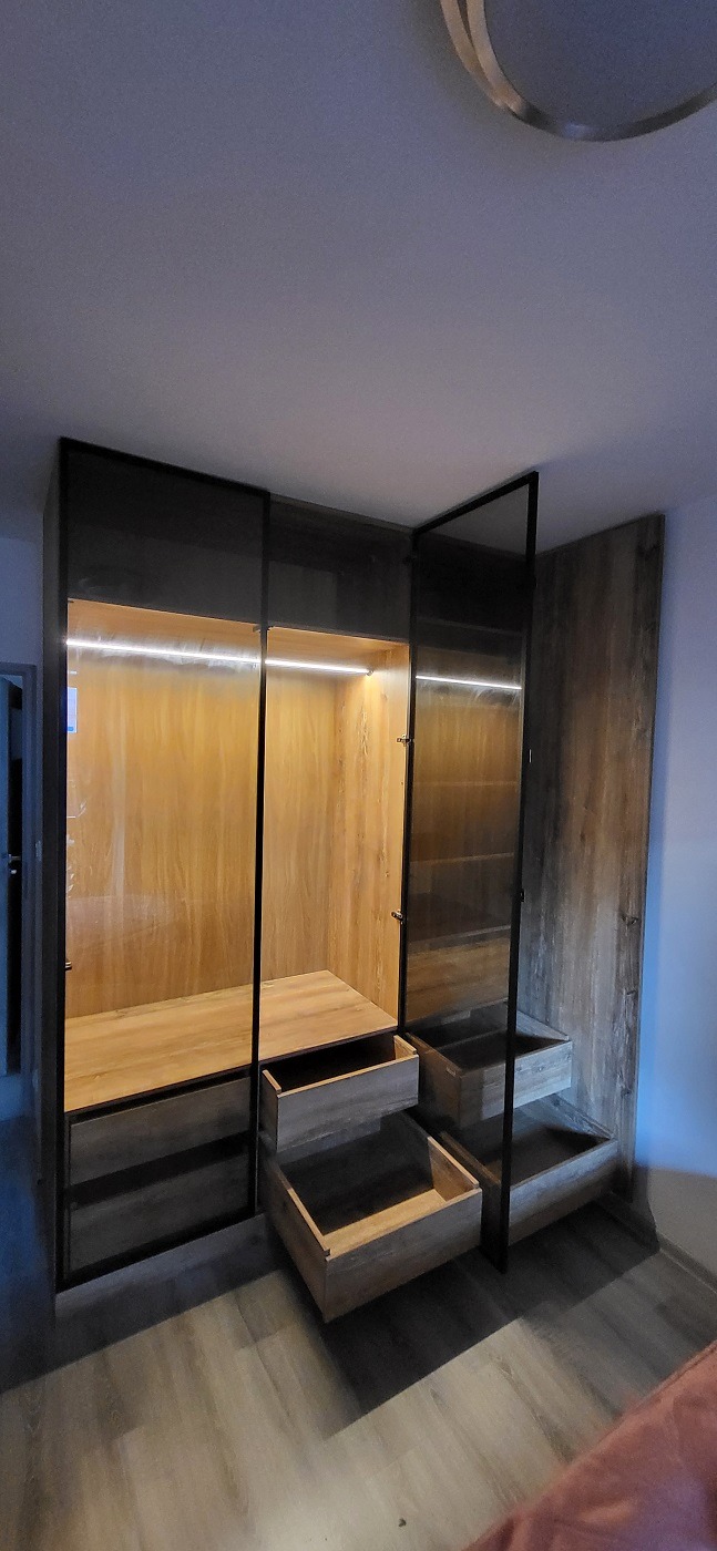 Nowoczesna szafa wnękowa z drewnianymi frontami, podświetleniem LED i otwartymi szufladami, widok z dołu.