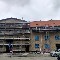 Remonty i ogrodnictwo - Dwa budynki z cegły, jeden z rusztowaniem, drugi z podnośnikiem, okna zabezpieczone folią, prace na wysokościach w toku.